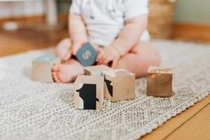 Baby sitzt auf dem Boden und hat einige Holzbausteine vor sich. Das ist ein Beispiel was in meiner Krabbelgruppe gemacht wird.